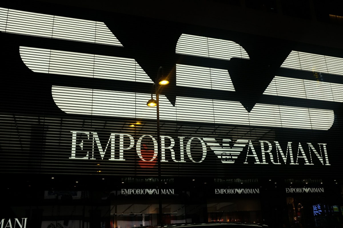 Illuminated Emporio Armani logo on a modern facade at night with geometric slats and a glowing streetlamp.