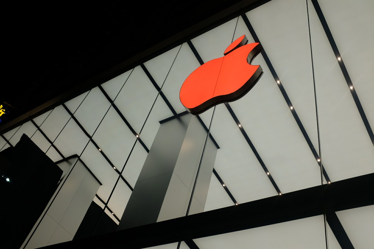 Low-angle night shot of a glowing red Apple logo mounted on a geometric white architectural facade.
