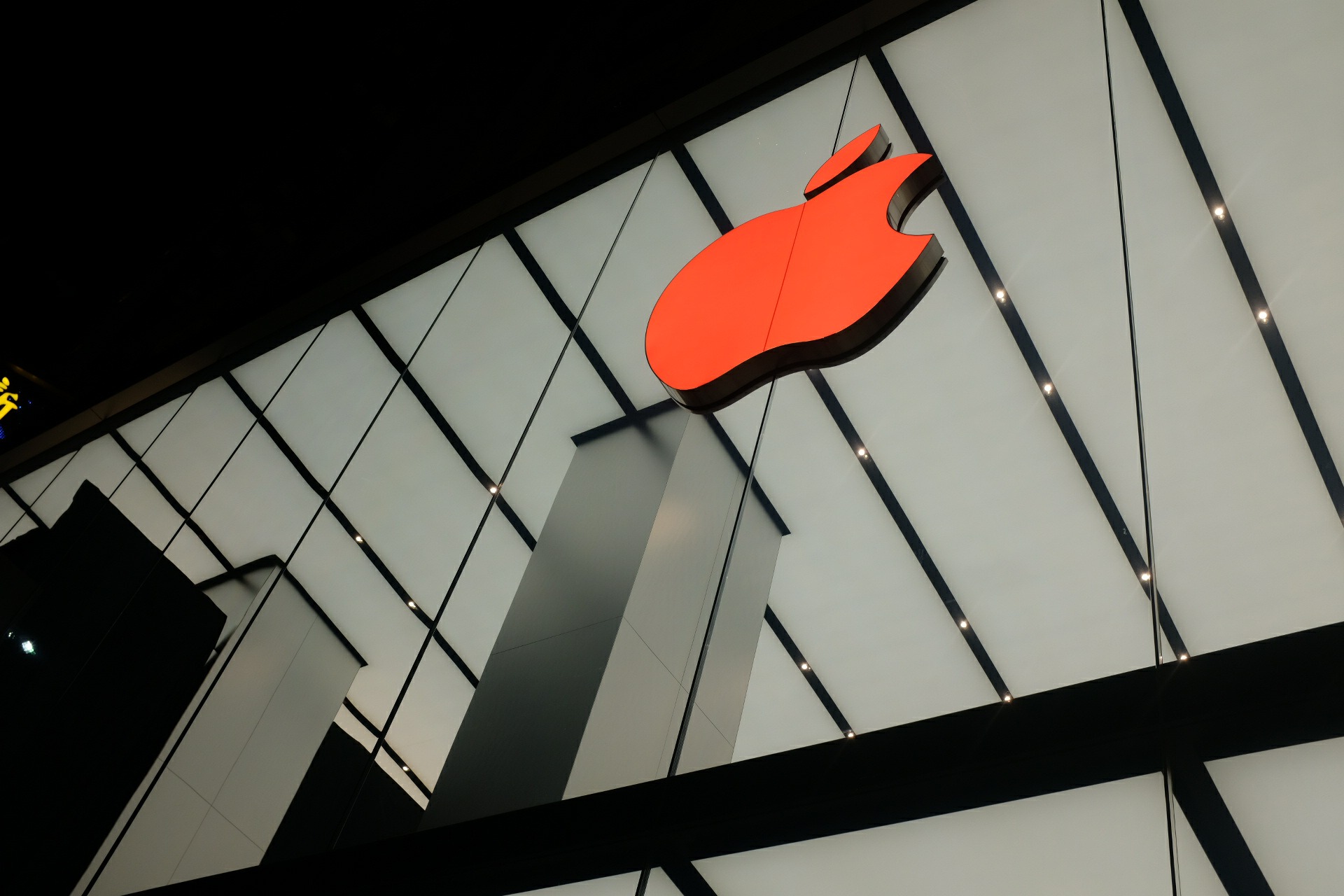 Low-angle night shot of a glowing red Apple logo mounted on a geometric white architectural facade.