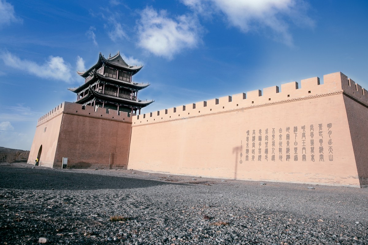 Low-angle view of the ancient Jiayuguan Pass gate tower on a fortified wall against a bright blue desert sky.