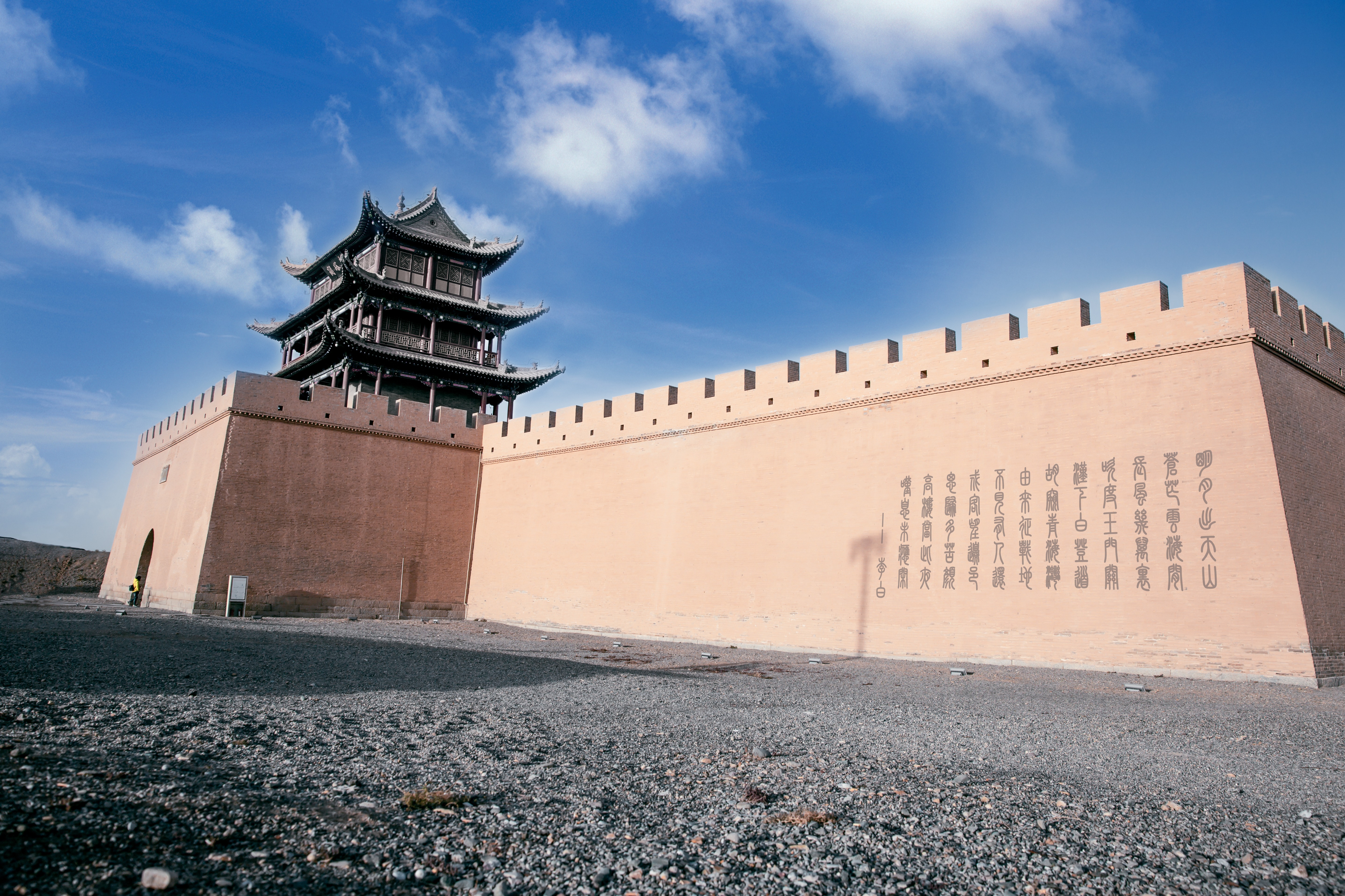 Low-angle view of the ancient Jiayuguan Pass gate tower on a fortified wall against a bright blue desert sky.