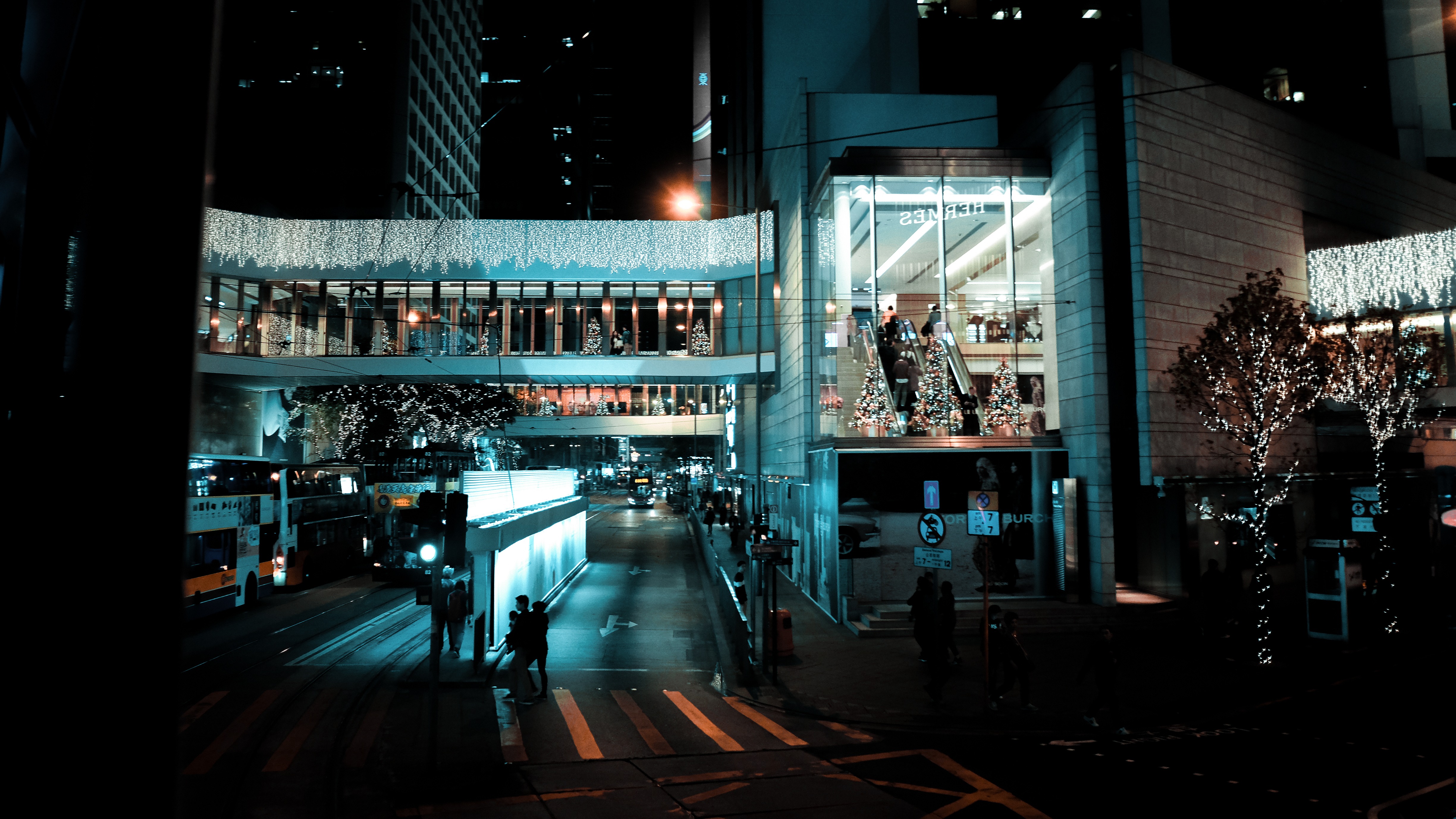 Tokyo intersection at night with illuminated pedestrian bridge, tram tracks, and glowing Hermès storefront.