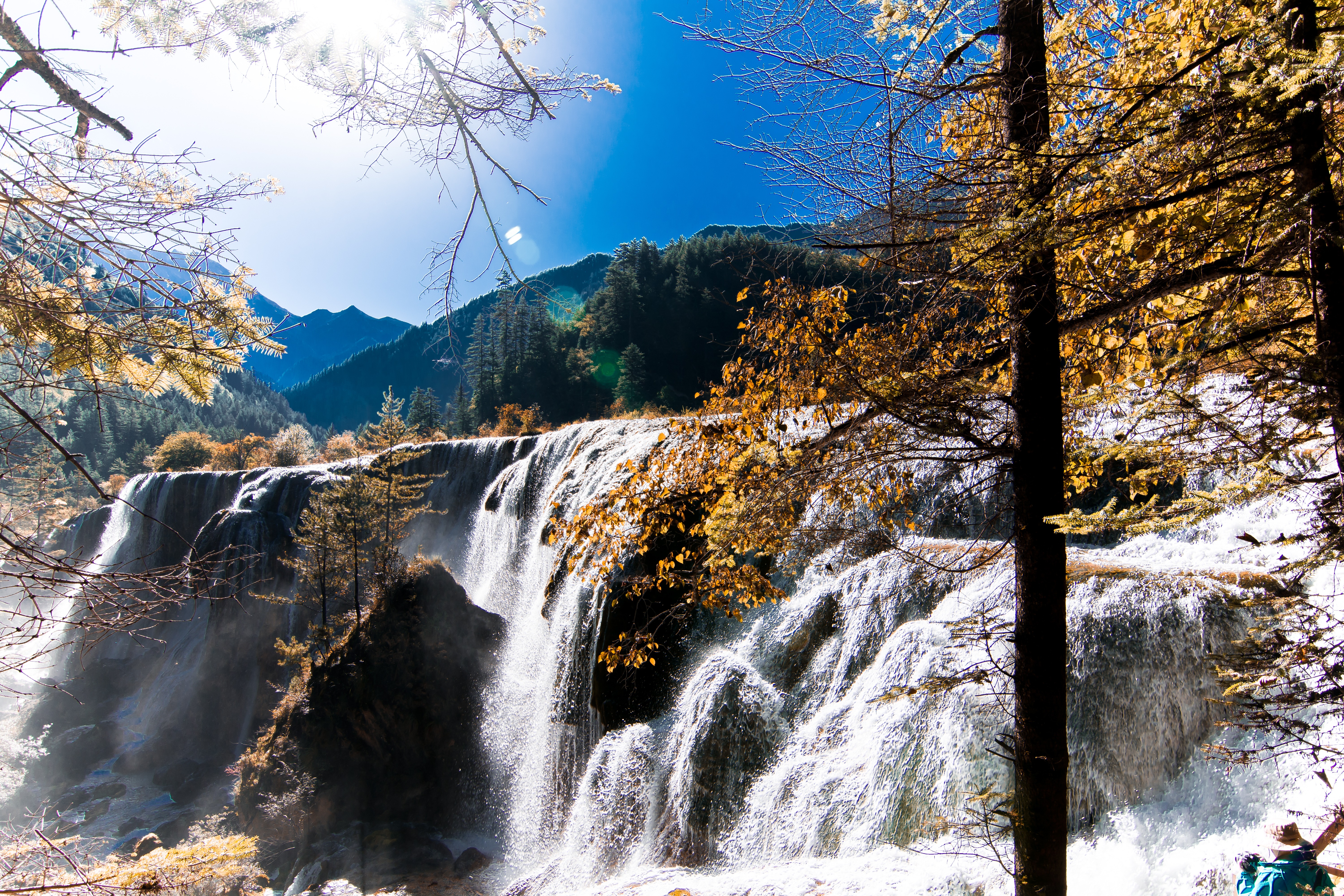 Multi-tiered waterfall cascading down a rocky cliff framed by golden autumn leaves in Jiuzhaigou Valley.