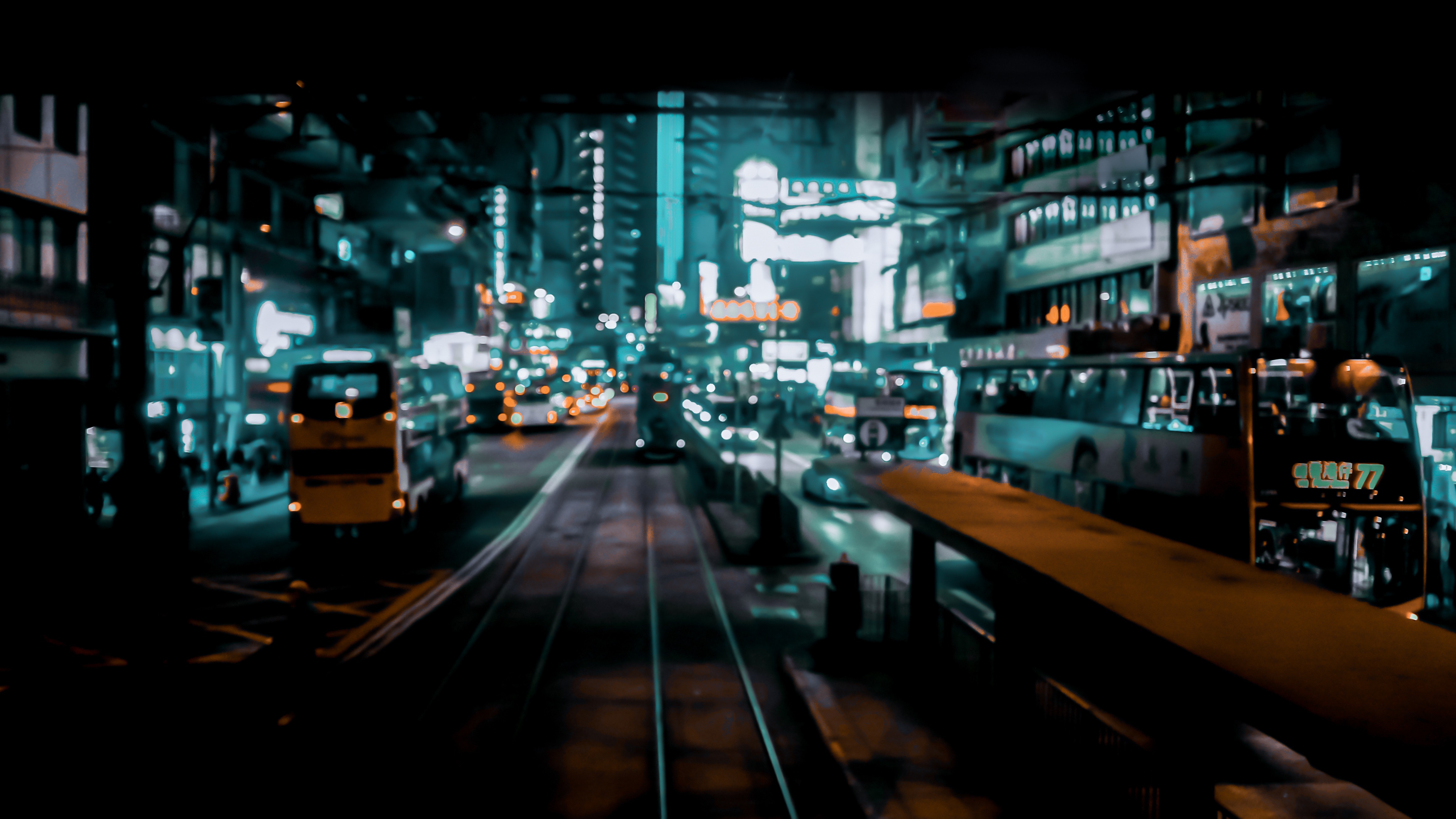 Night street scene in Hong Kong featuring glowing tram tracks leading past double-decker buses and neon storefronts.