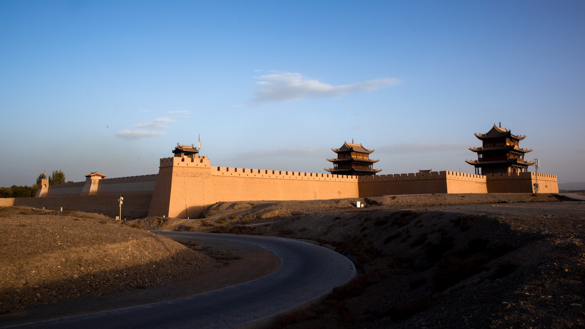 Ancient Chinese fortress wall with three watchtowers stretching across an arid desert landscape during golden hour.