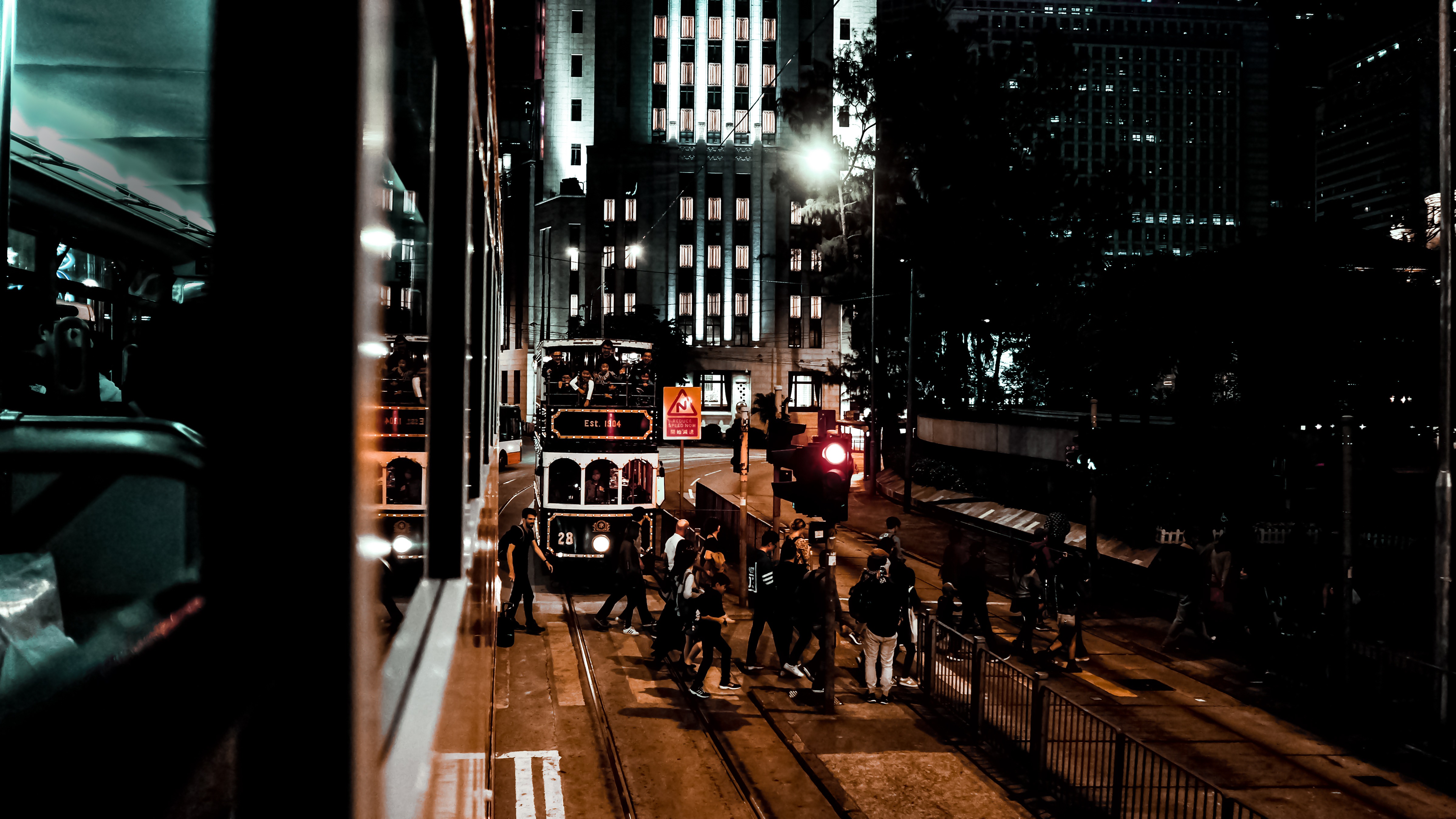Vintage double-decker tram glowing on a Hong Kong street at night, framed by towering buildings and glass reflections.