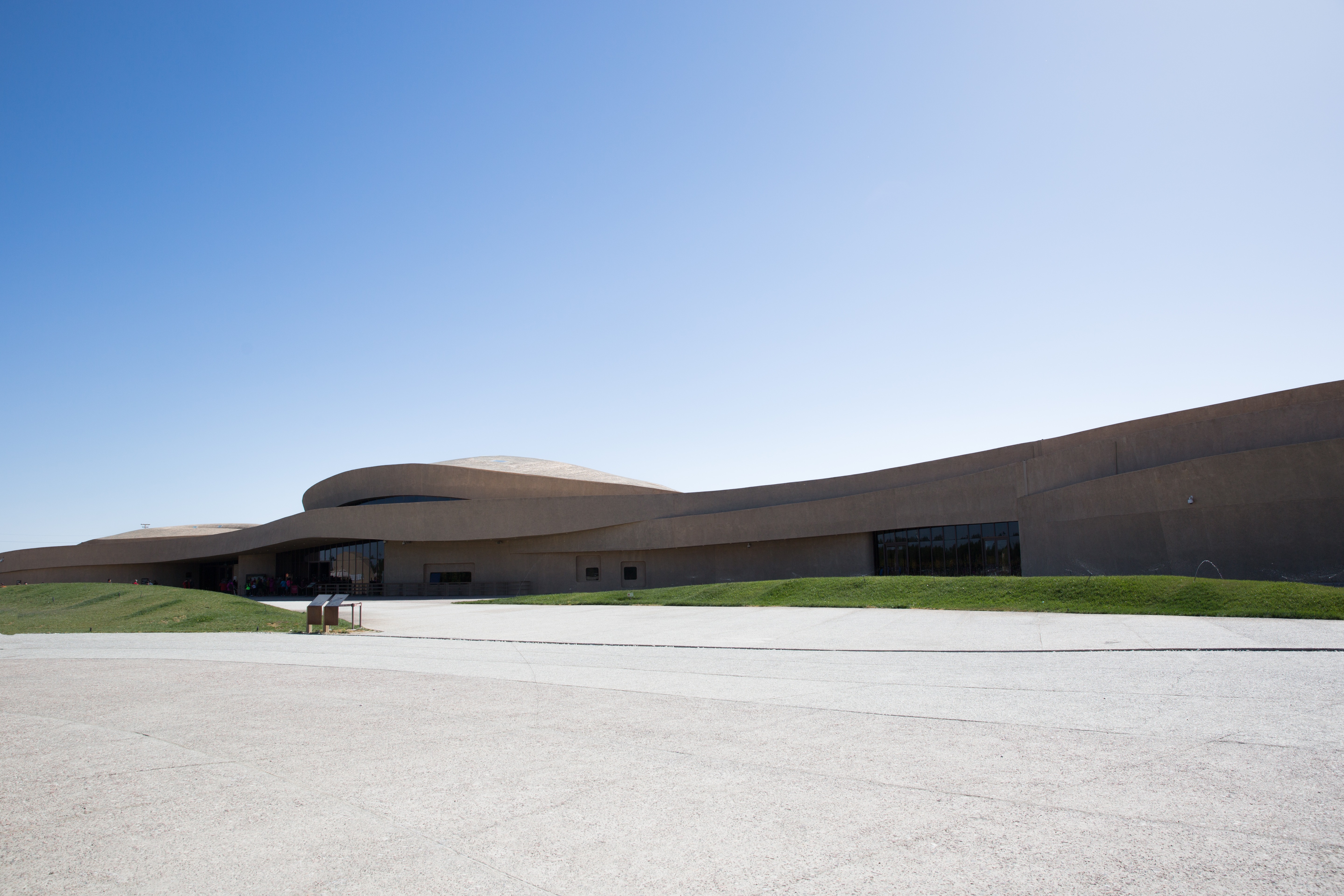 Curvilinear concrete building with sweeping curves on a flat plaza under a vast gradient blue sky.